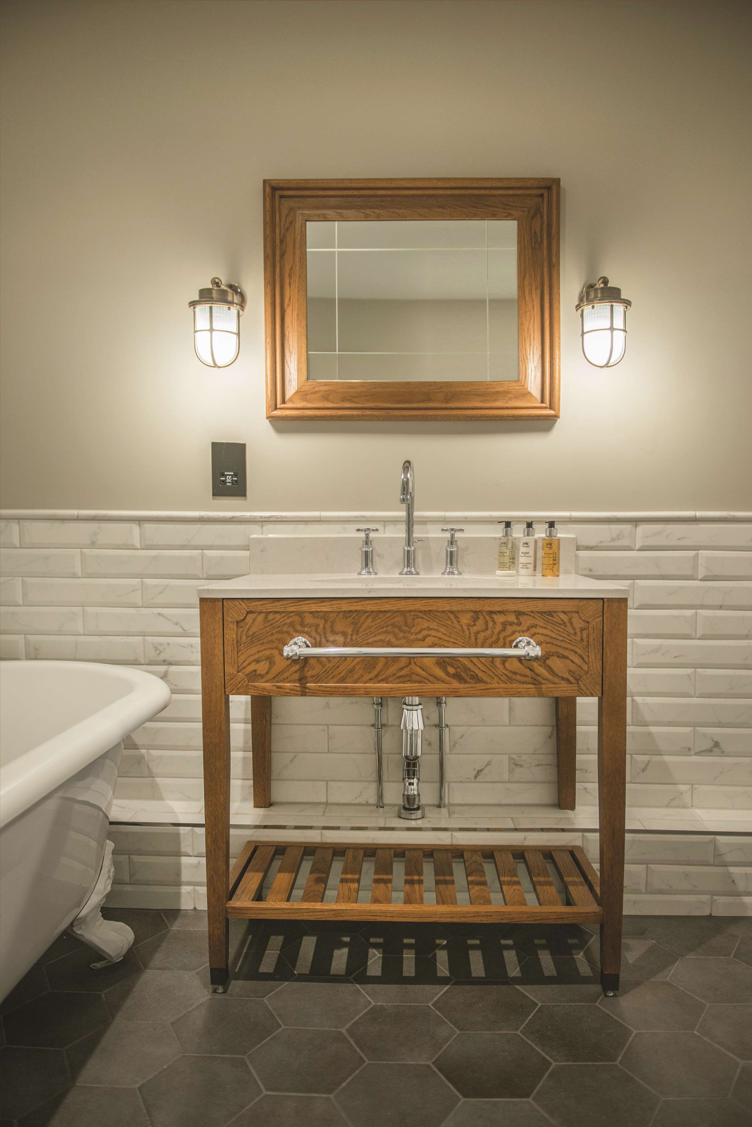 A bathroom with a wooden vanity, a white sink, and a large mirror above it. There are two wall-mounted lights on either side of the mirror.