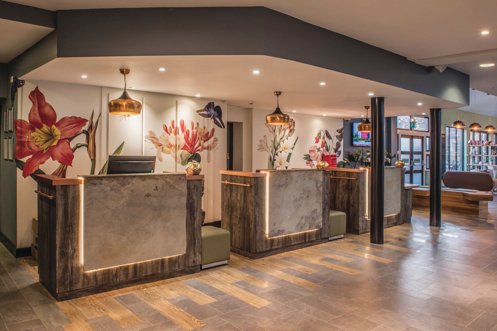 A reception area with wooden reception desks, a large floral mural, and a television screen.