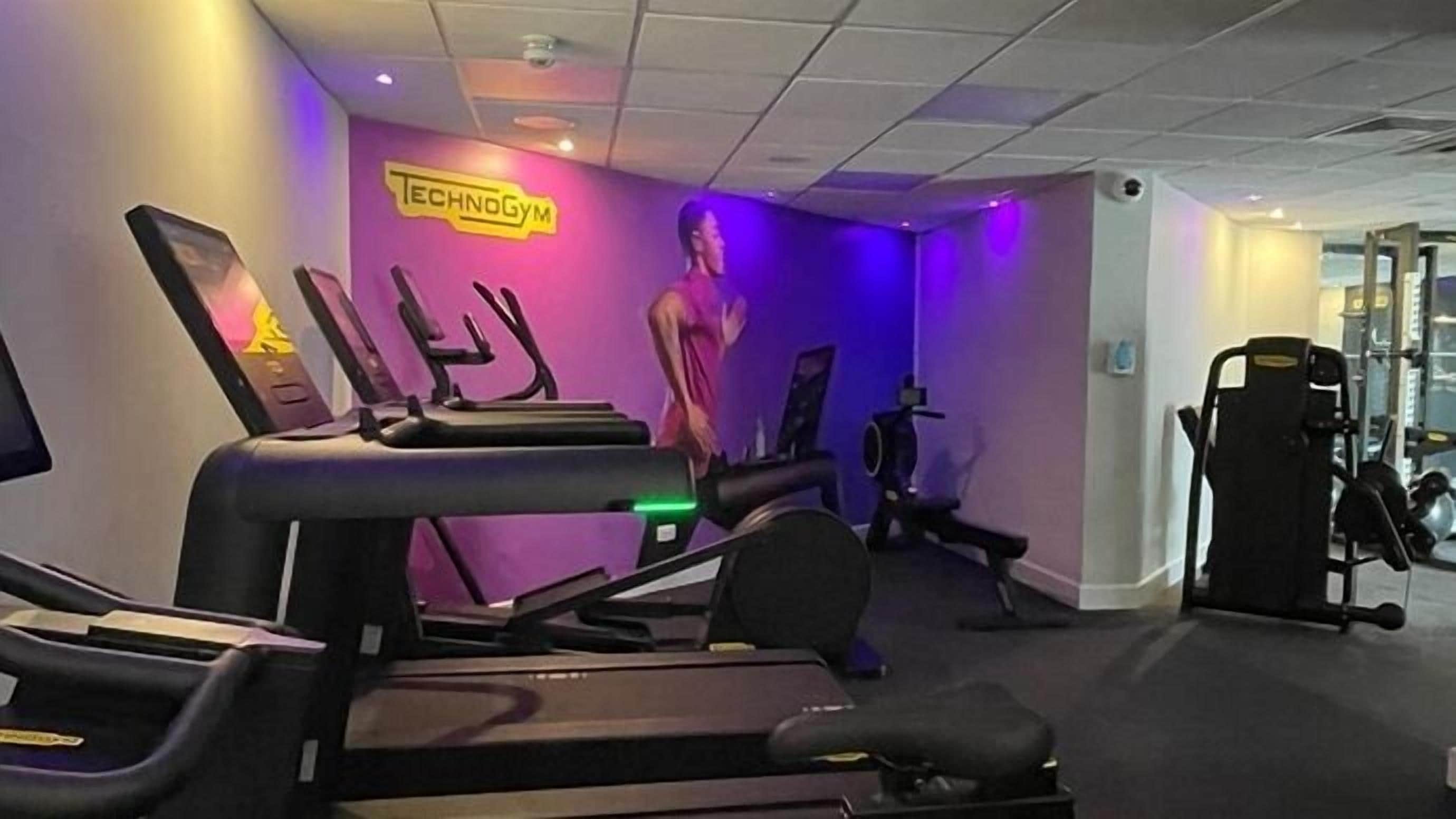 Une salle de sport équipée de tapis de course, d’un appareil d’exercice fixé au mur et d’un miroir.