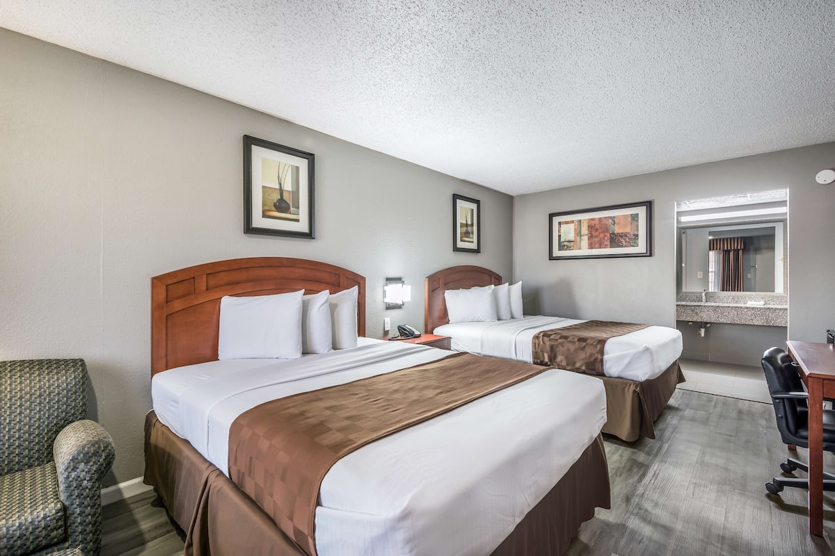 A hotel room with two beds, a desk, a chair, and framed artwork on the walls.