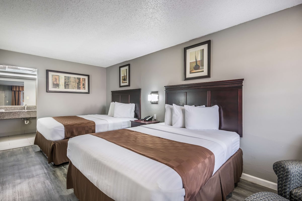 A hotel room with two beds, a desk, a chair, and a bathroom visible through an open door.
