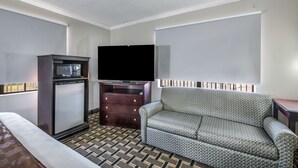 A hotel room with a bed, a sofa, a small kitchenette with a microwave, a TV, and a patterned carpet. - Americas Best Value Inn & Suites Arkadelphia (Arkadelphia)