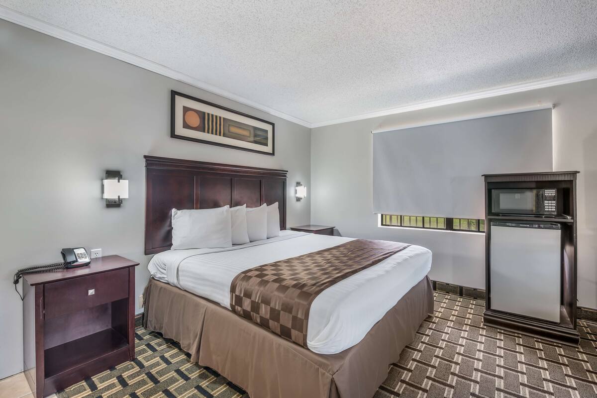 A hotel room with a large bed, a nightstand with a phone, a wall-mounted TV, and a refrigerator.