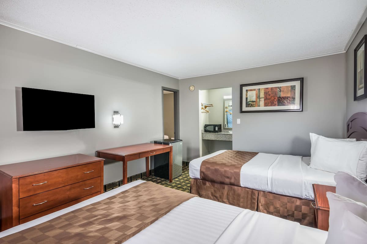A hotel room with two beds, a desk, a dresser, a flat-screen TV, a framed artwork, and a bathroom visible through an open door.