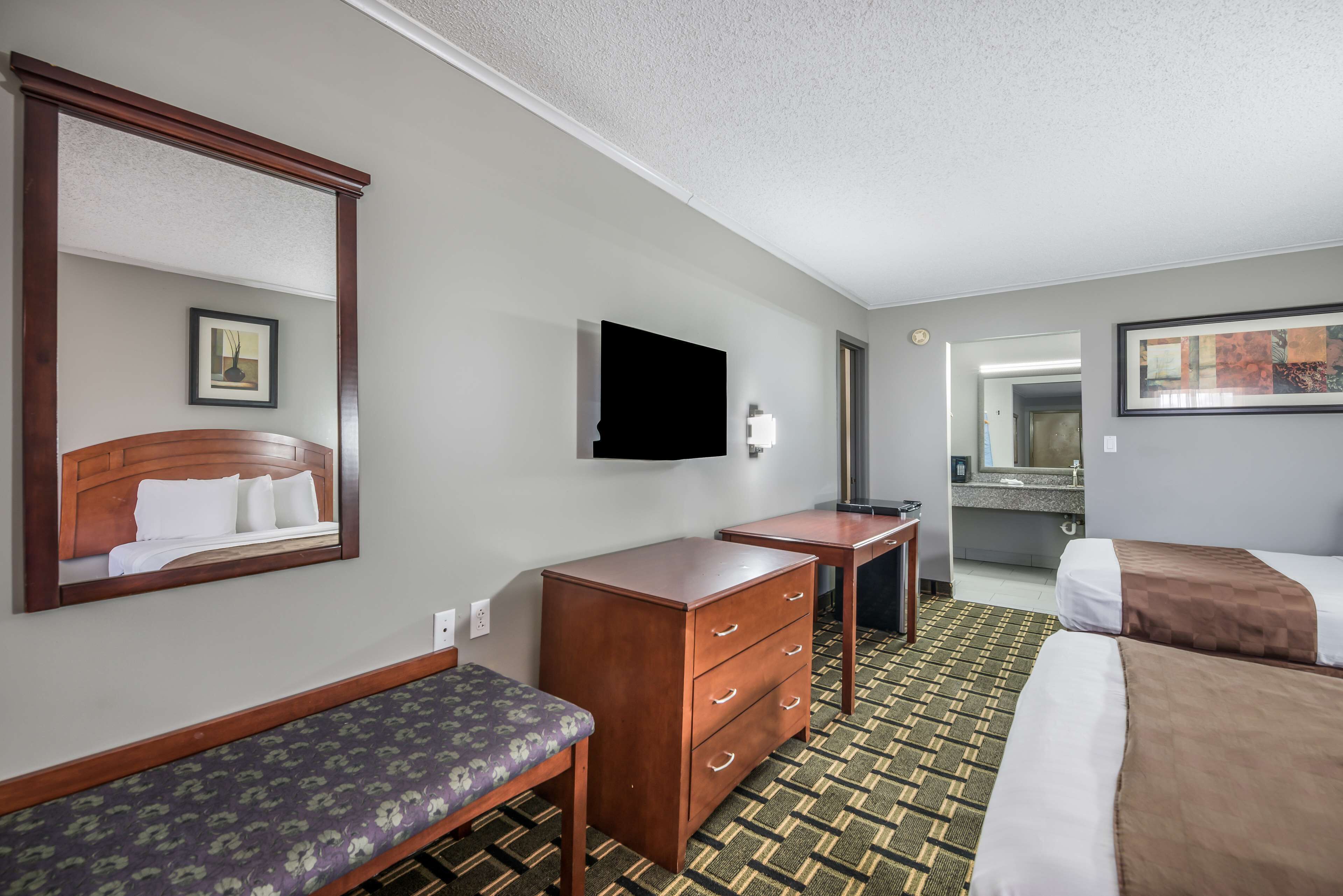 Habitación de hotel con cama, una banca, cómoda, televisor y baño visible a través de una puerta abierta.