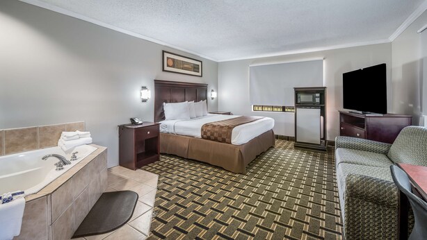 A hotel room with a bed, a desk, a chair, a TV, a microwave, and a bathroom with a bathtub and sink. - Americas Best Value Inn & Suites Arkadelphia (Arkadelphia)