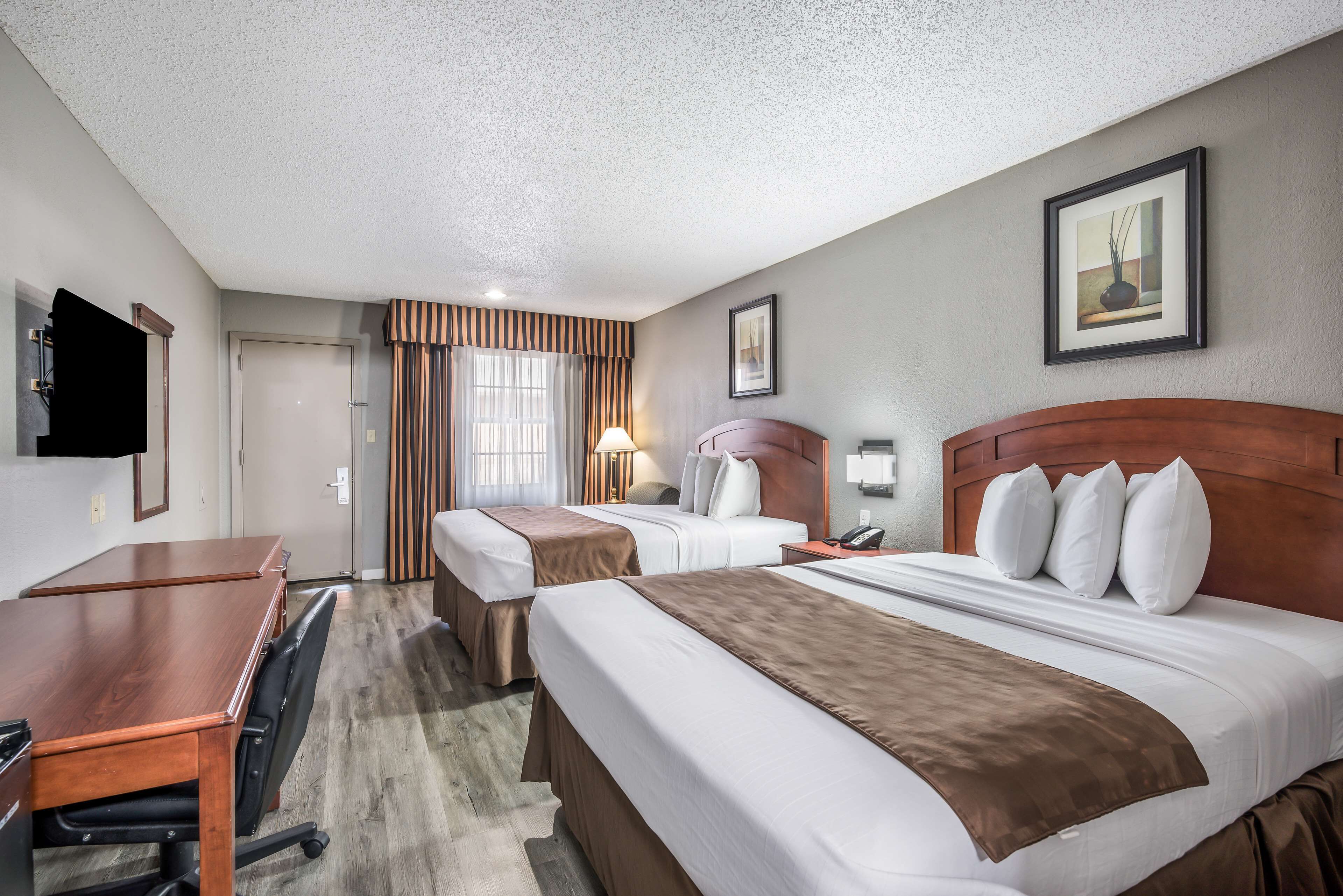 A hotel room with two beds, a desk, and a chair.