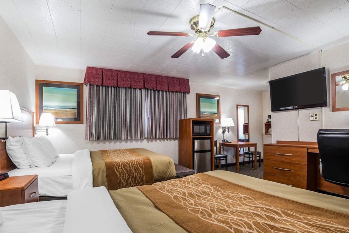 Habitación de hotel con dos camas, ventilador de techo, televisor, escritorio con silla, microondas y refrigerador.