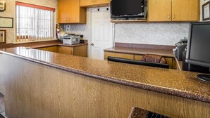 A kitchen with wooden cabinets, a countertop, a television, and a door. - Rodeway Inn Elko Downtown Area (Elko)