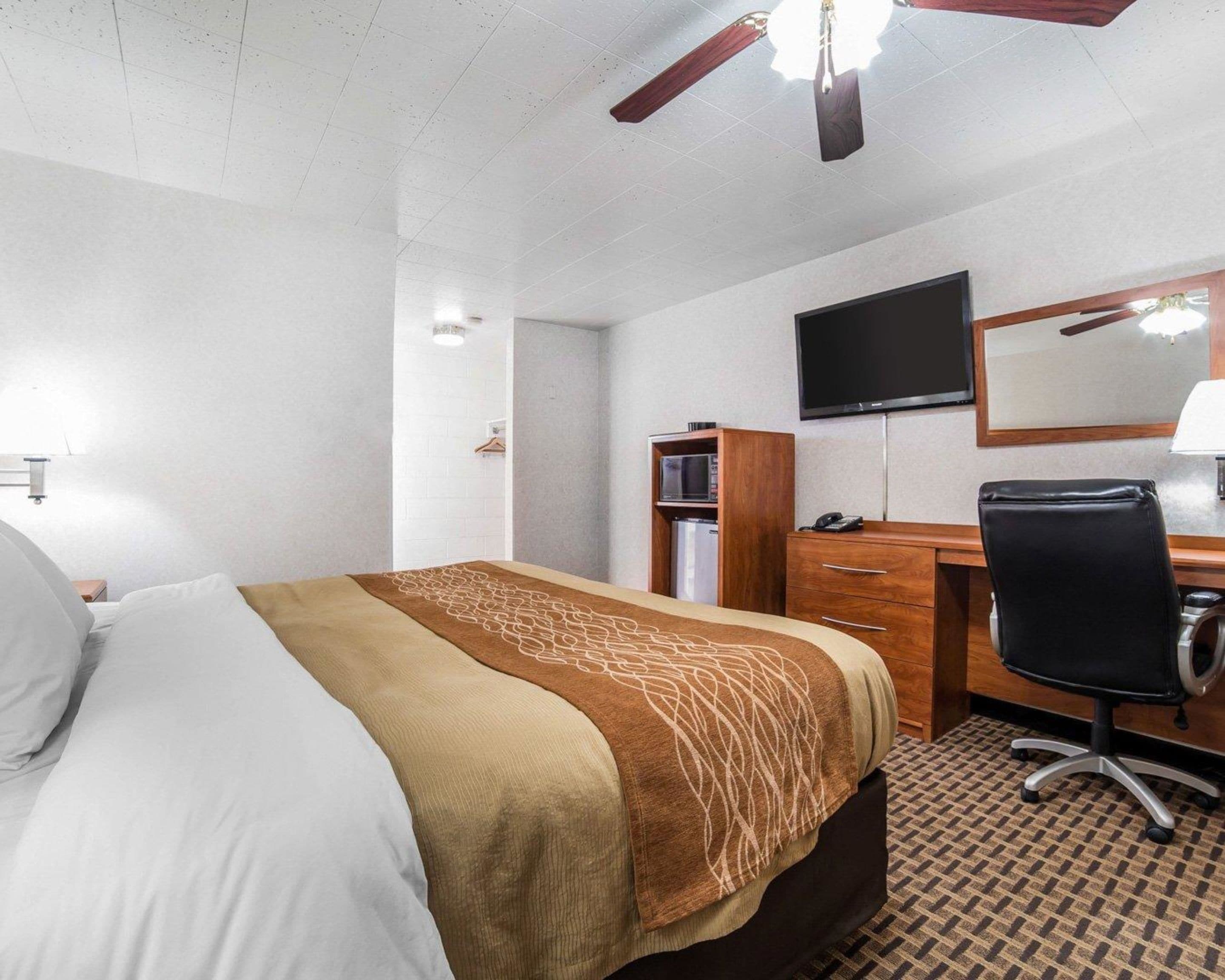 A hotel room with a bed, a desk, a chair, a television, and a wardrobe.