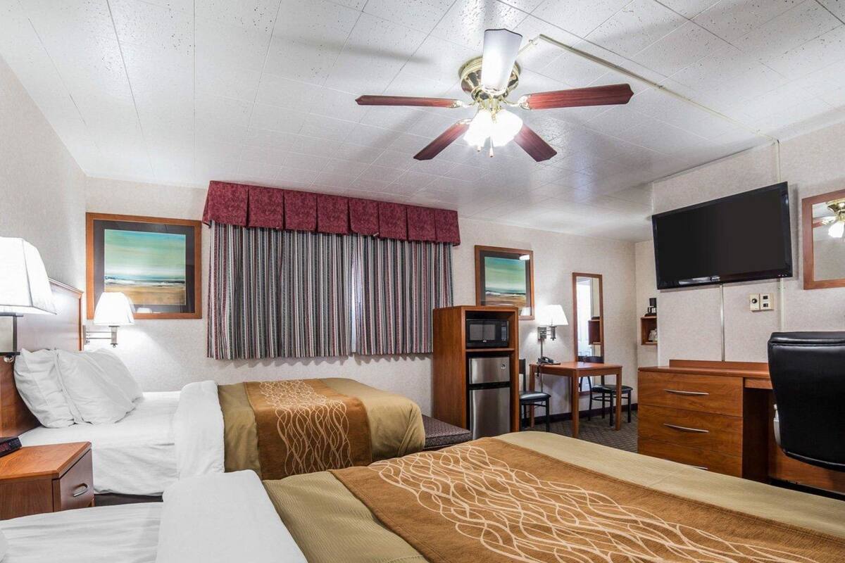 Una habitación de hotel con dos camas, un escritorio, televisor, microondas y ventilador de techo.