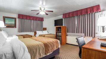 Quarto de hotel com duas camas, uma escrivaninha, uma cadeira, uma televisão e um ventilador de teto.