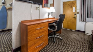 A hotel room with a wooden desk, a black office chair, a flat-screen TV mounted on the wall, a mirror above the desk, a lamp, a door with a wooden frame, and a patterned carpet. - Rodeway Inn Elko Downtown Area (Elko)