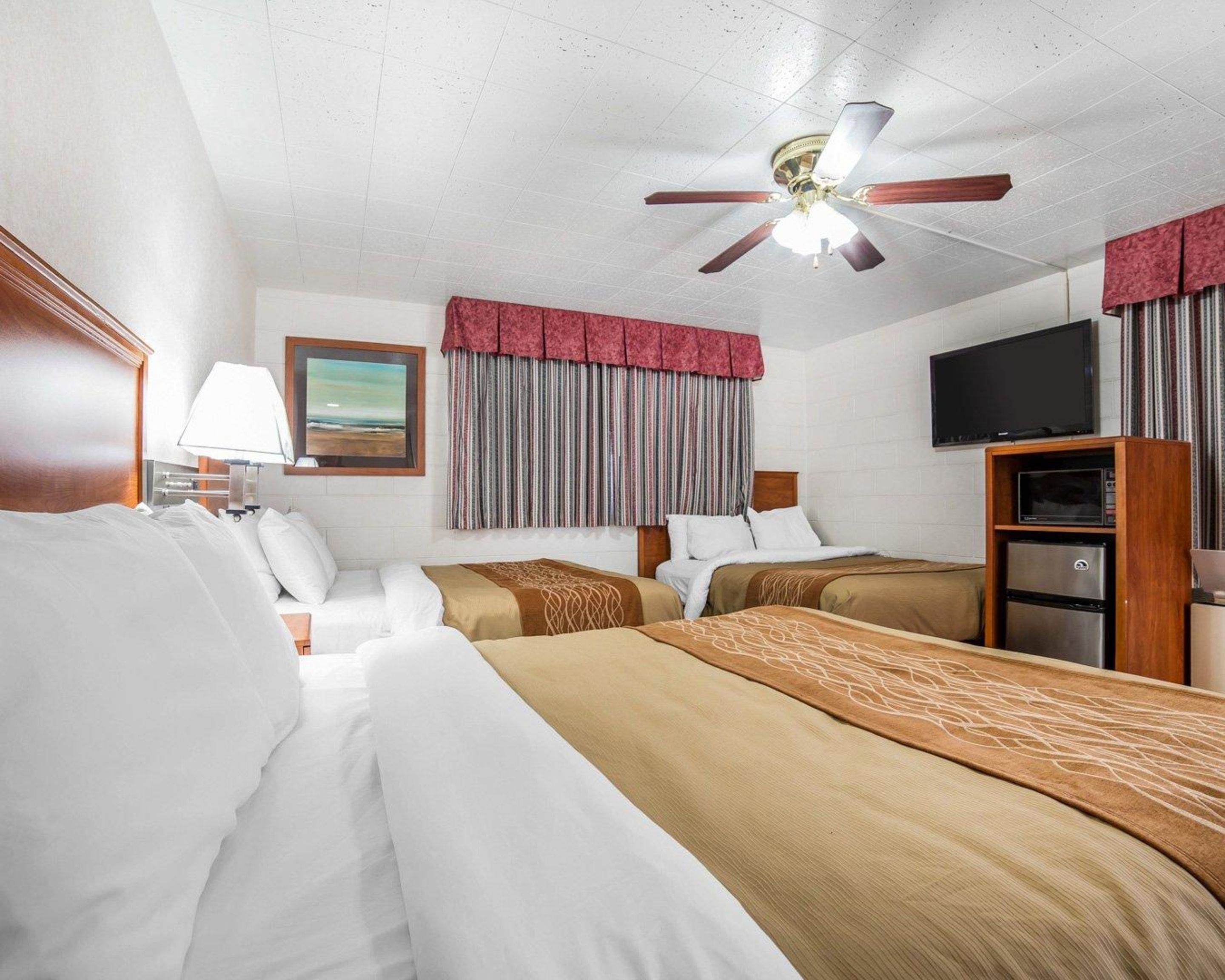 A hotel room with two beds, a ceiling fan, a television, and a minibar.