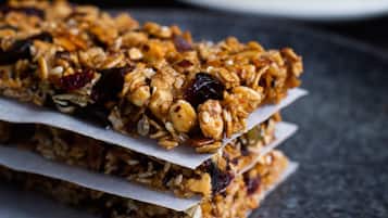 A stack of granola bars on a dark plate with a cup of coffee in the background.