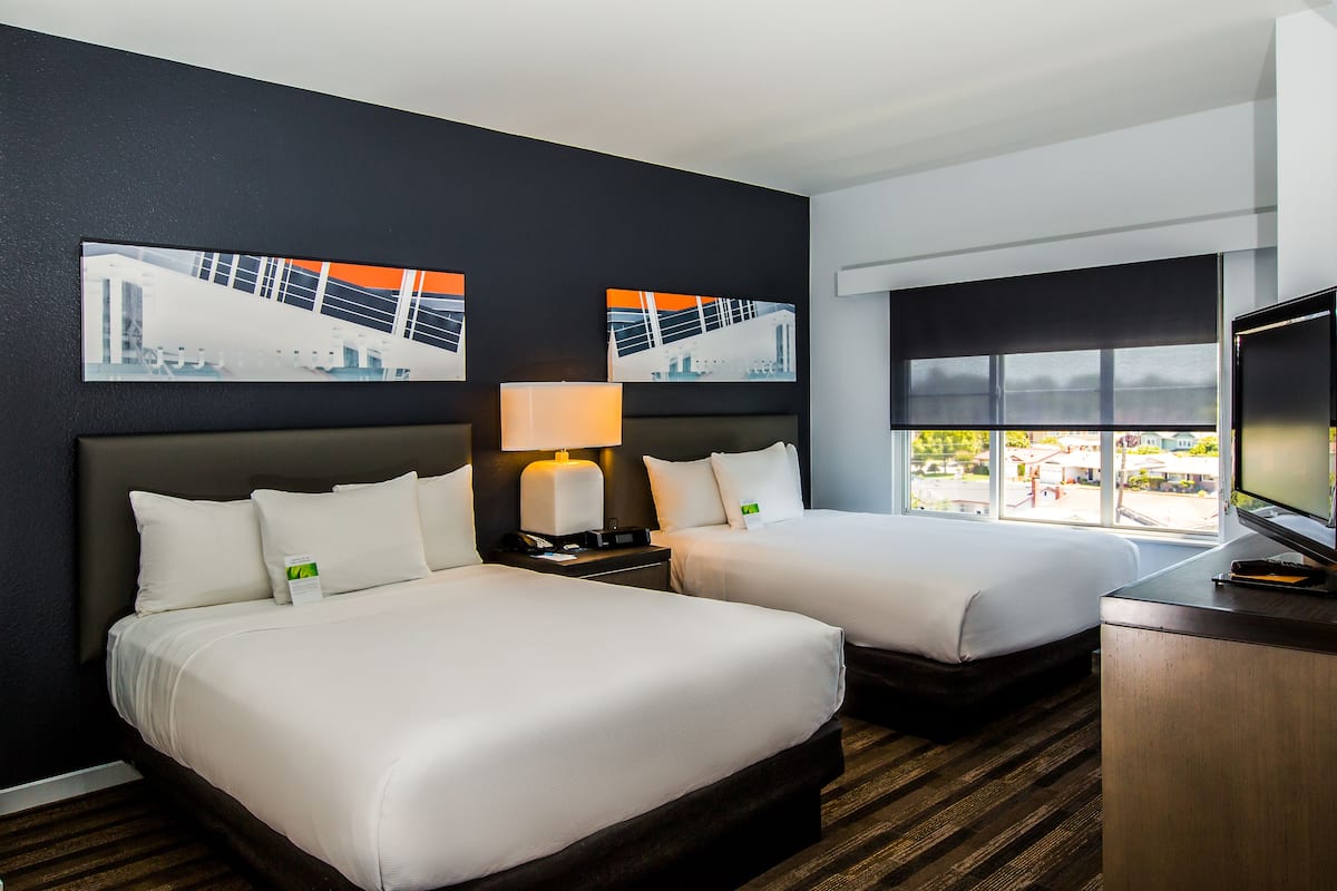 A hotel room with two beds, a desk, a TV, and a window with a view.