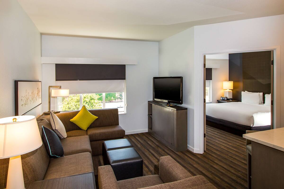 A hotel room with a sofa, ottomans, a flat-screen TV, a bed, and a desk.