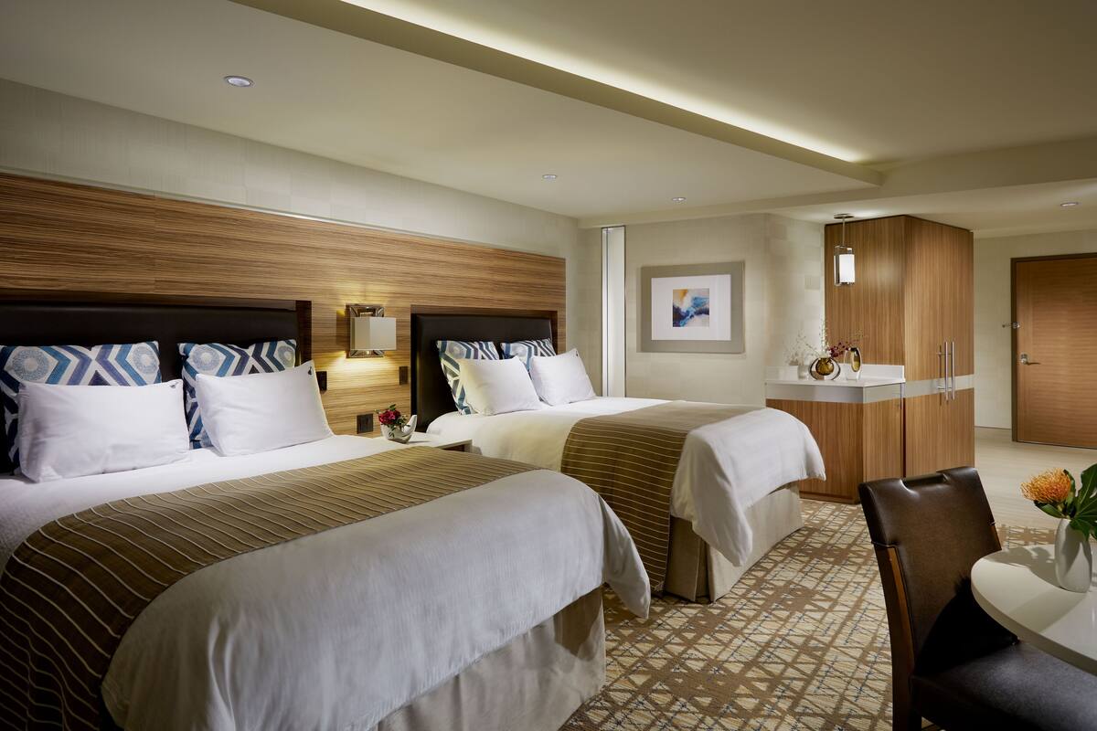 Une chambre d’hôtel avec deux lits, une tête de lit en bois, une petite table avec un vase et une armoire.