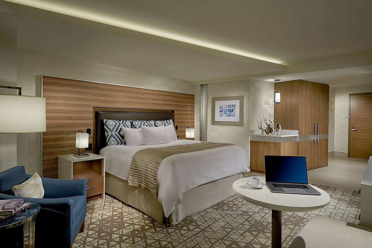 Une chambre d’hôtel moderne avec un grand lit, un bureau avec un ordinateur portable, une chaise et une petite table avec une tasse.