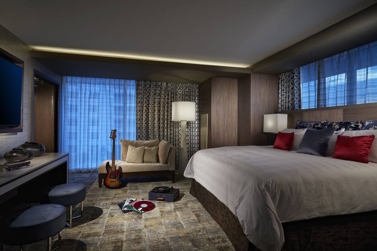 Une chambre d’hôtel avec un lit, un bureau et une chaise, un canapé et une guitare.