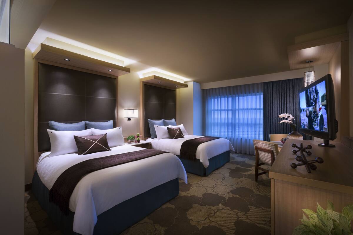 Une chambre d’hôtel avec deux lits, un bureau avec une télévision et une grande fenêtre avec des rideaux.