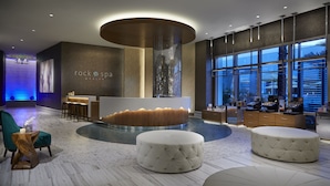 A modern spa and salon interior with a central reception desk, seating area, and large windows.