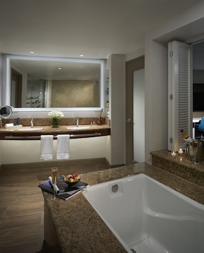 A modern bathroom with a large bathtub, granite countertops, a mirror, and a shower area.