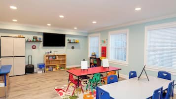 A brightly lit room with a red table, blue chairs, a whiteboard, and a television on the wall.
