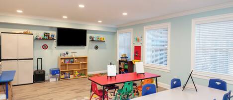 Una habitación luminosa con una mesa roja, sillas azules, una pizarra y un televisor en la pared.