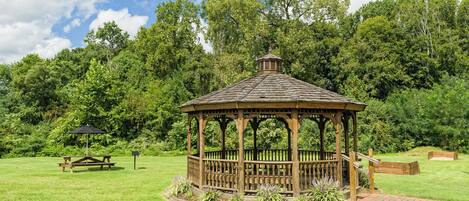 Un gazebo de madera con techo, rodeado de césped y árboles.