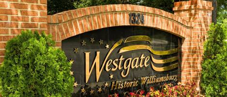 Un arco de ladrillo con el cartel Westgate Historic Williamsburg, rodeado de vegetación.