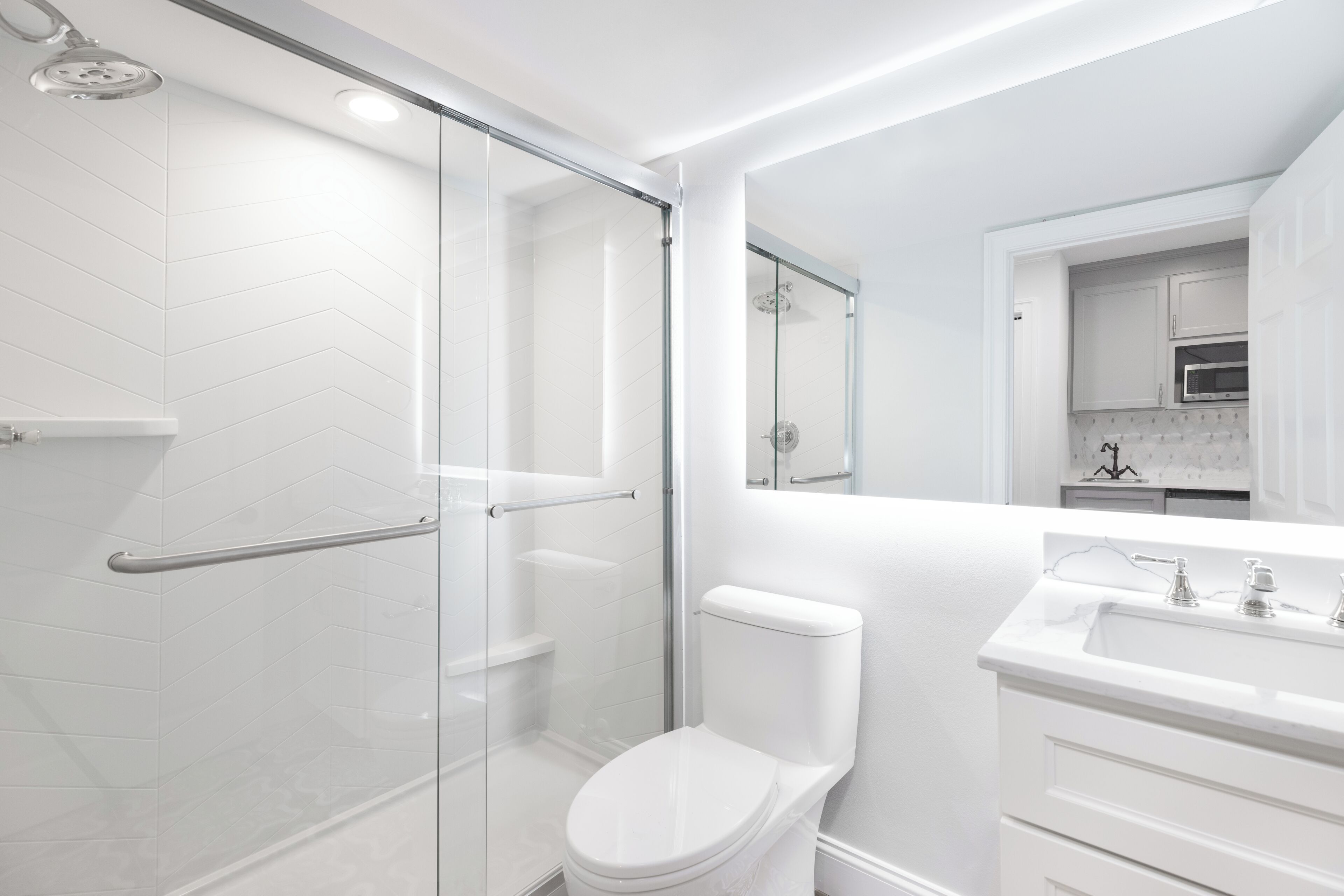 A modern bathroom with a glass shower enclosure, a white toilet, and a vanity with a mirror.