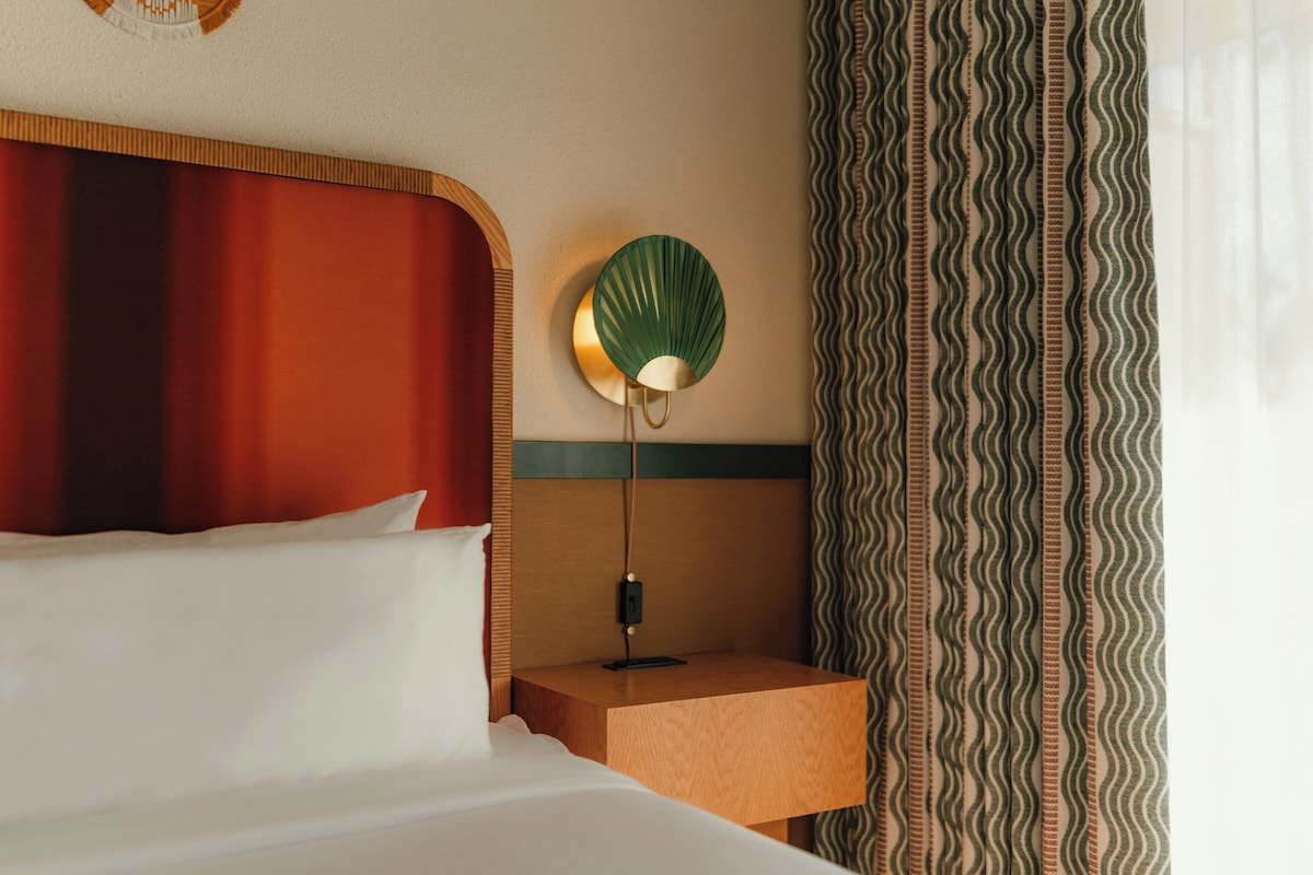 Une chambre d’hôtel avec un lit, une table de chevet avec une lampe et un rideau à motifs.