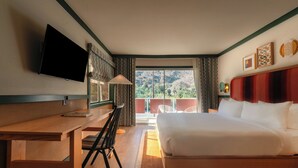 A hotel room with a bed, a desk, a television, and a view of the outdoors.