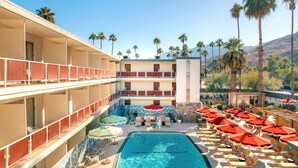 Ein Hotel mit Pool, mehreren Etagen, Außenbereich, Palmen und Bergen im Hintergrund.