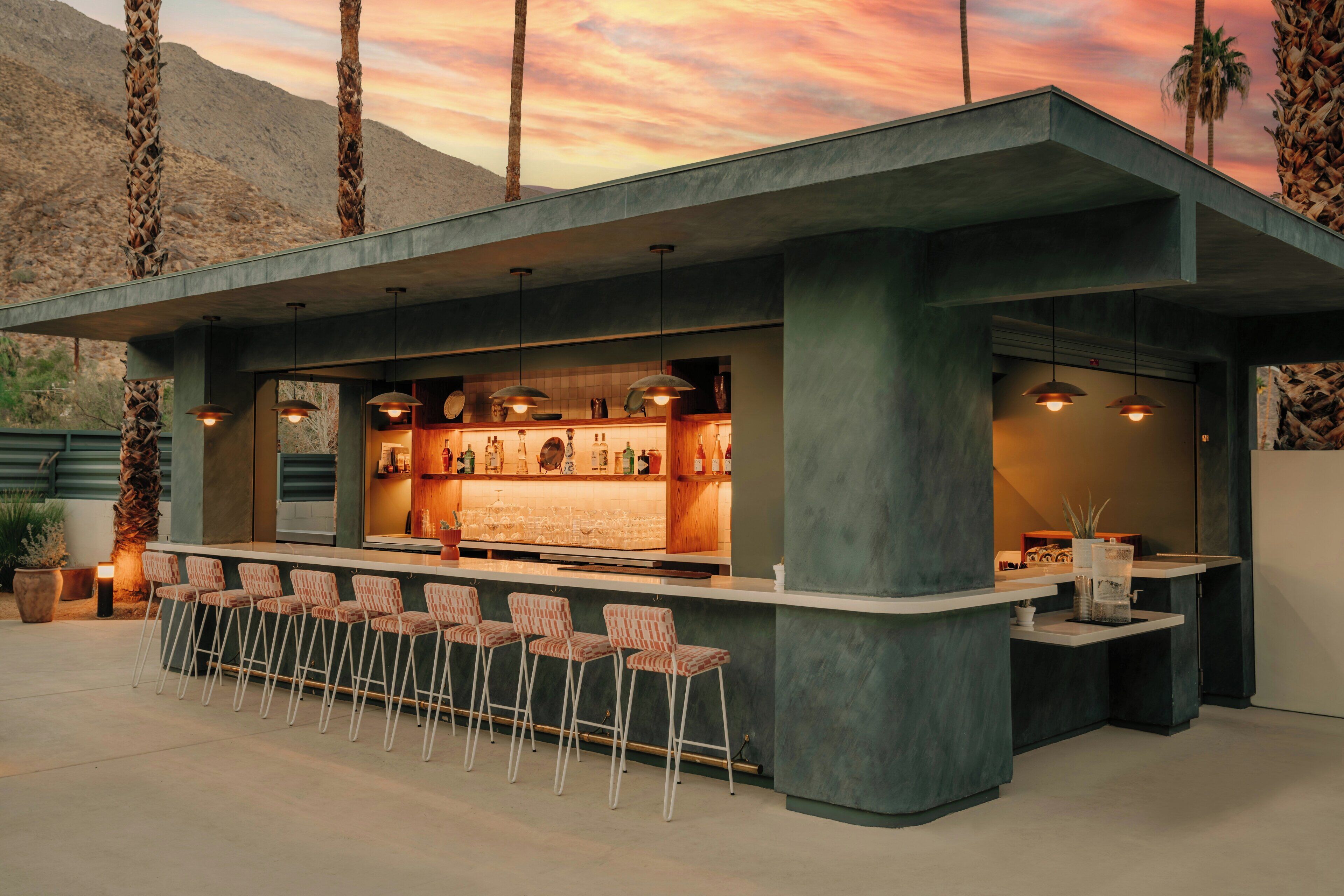 An outdoor bar area with a concrete structure, bar stools, and pendant lighting.