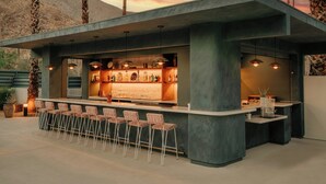 An outdoor bar area with a concrete structure, bar stools, and pendant lighting.