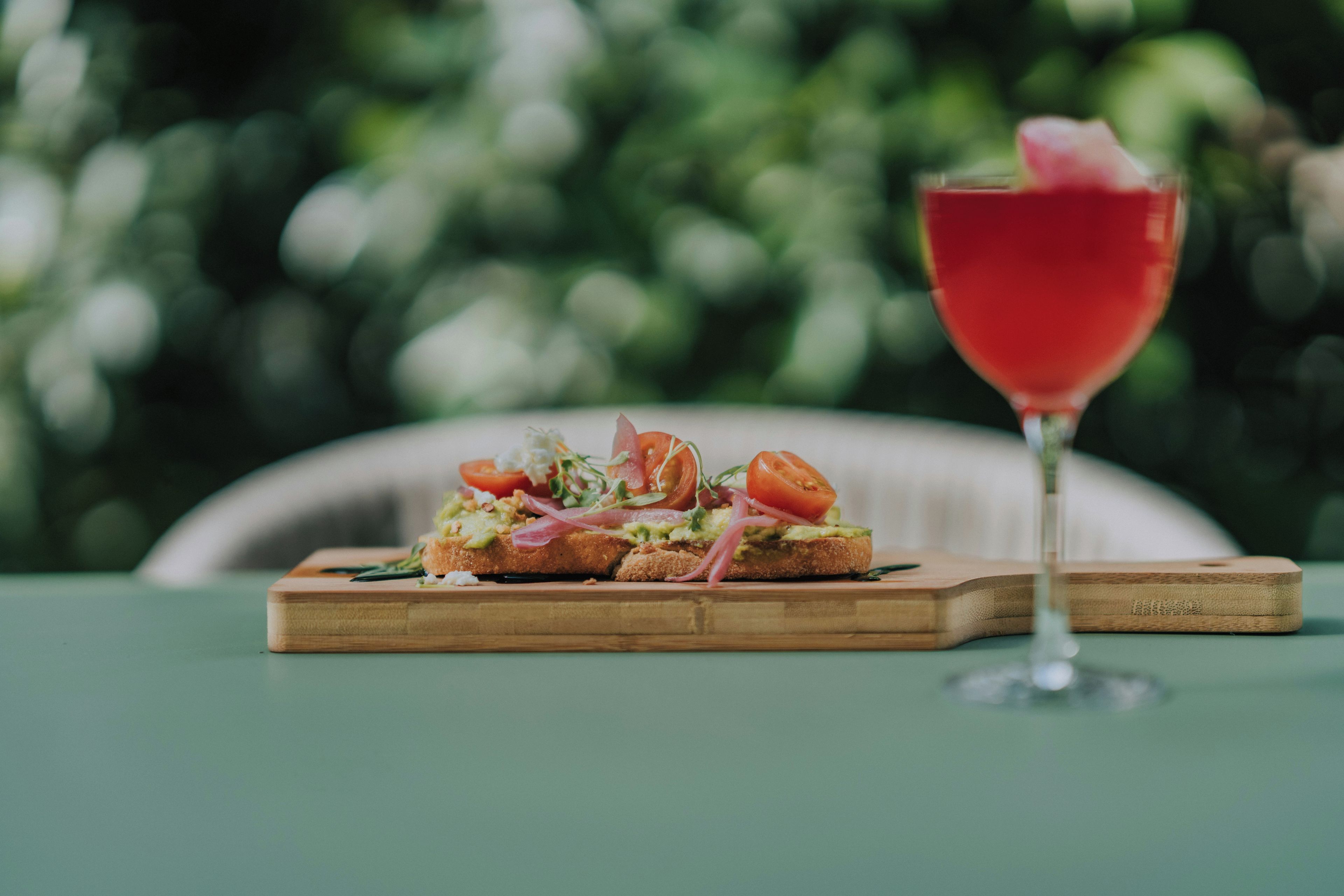 A wooden board with a dish of food and a glass of red beverage on a table.