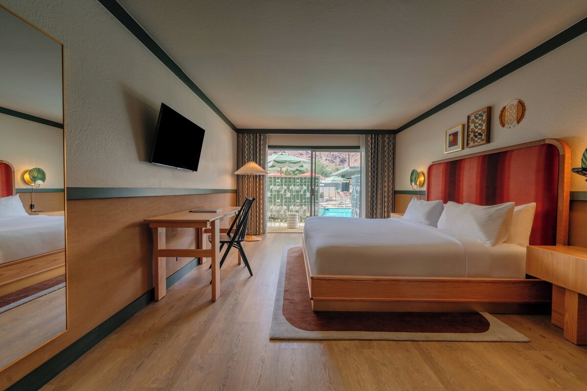 A hotel room with a bed, a desk, a chair, a television, and a view of the outdoors.
