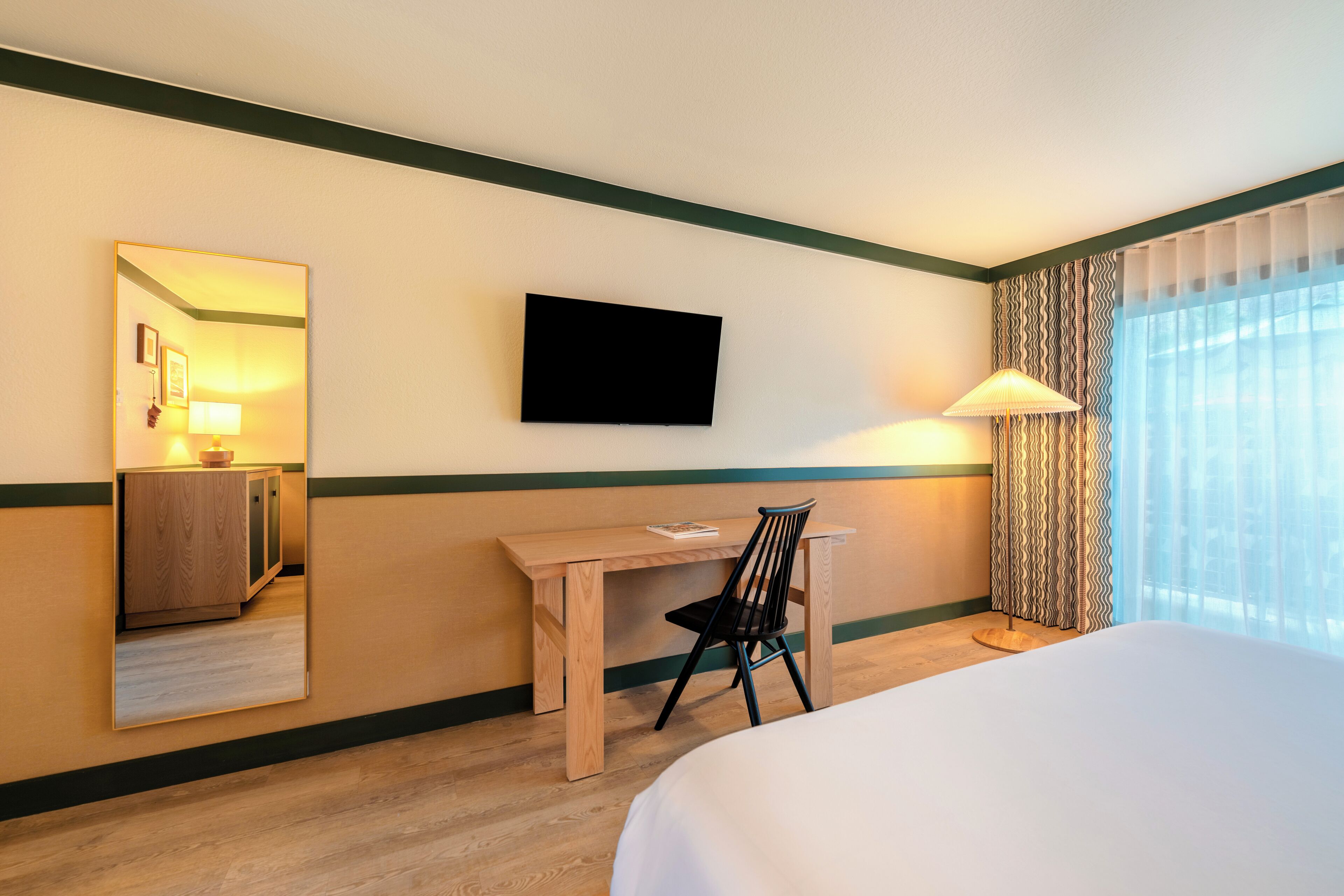 A hotel room with a bed, a desk, a chair, a TV, and a window with curtains.