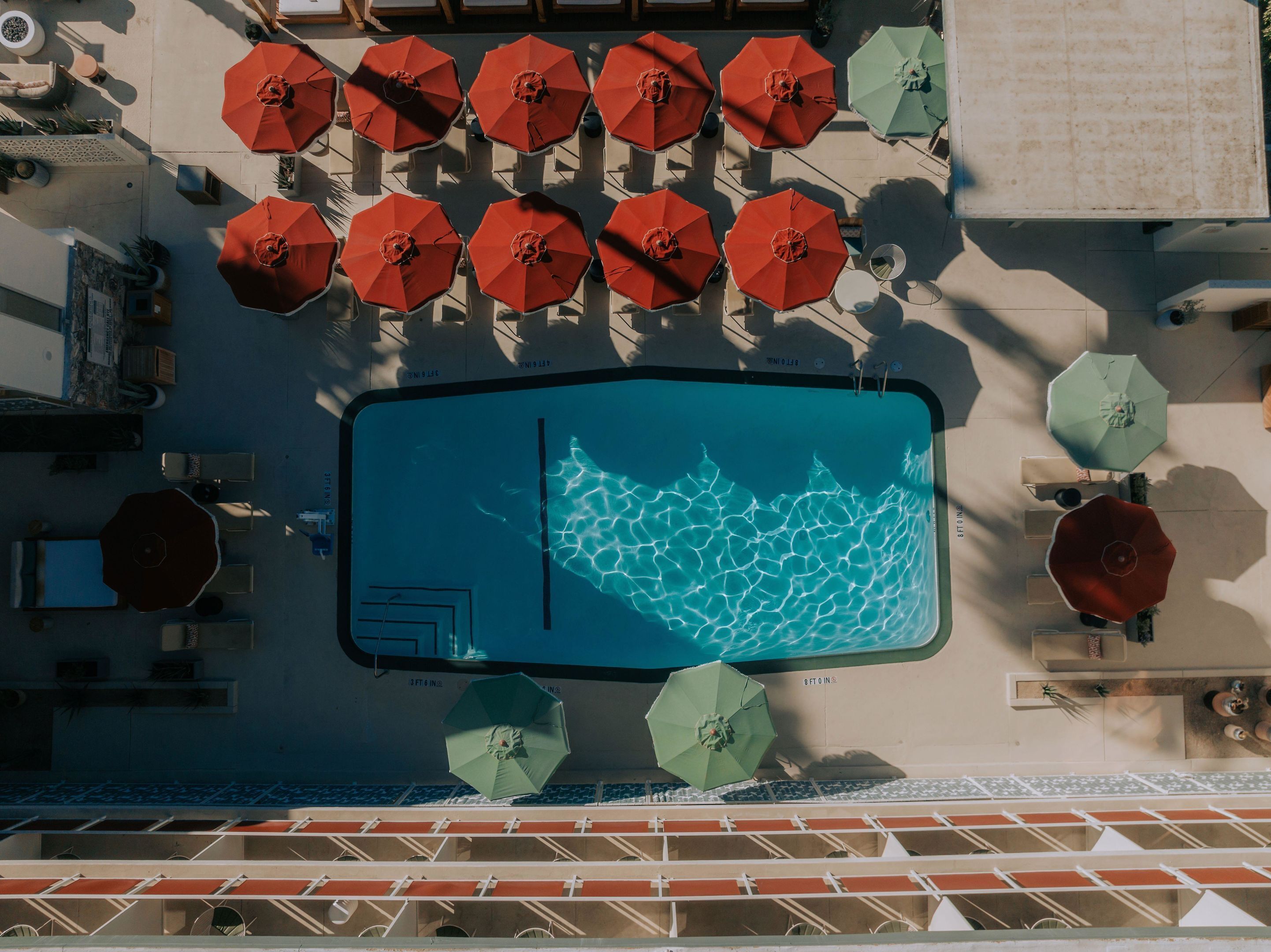Uma área de piscina com vários guarda-sóis, cadeiras de descanso e uma piscina com água cristalina.
