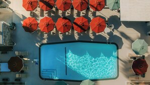 A rooftop pool with multiple red umbrellas and lounge chairs arranged around it.