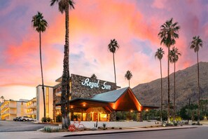 Un hotel con fachada de piedra, llamado 'Royal Sun', presenta un diseño moderno con una entrada destacada y palmeras en primer plano.