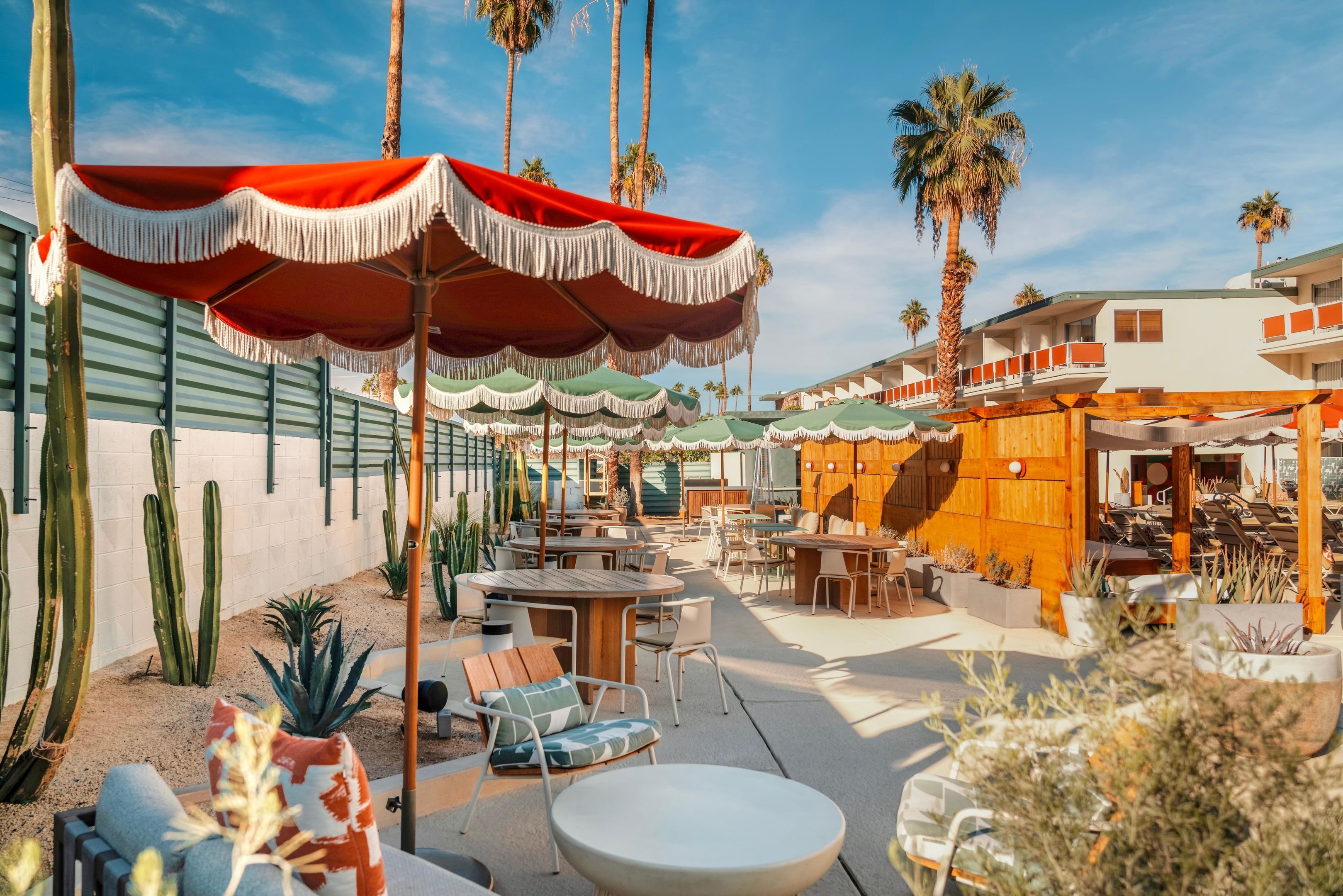 Eine Außenpatio-Terrasse mit Tischen, Stühlen, Palmen und einem Gebäude mit Holzfassade.