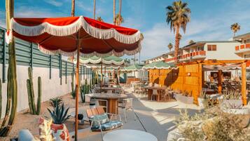 Eine Außenpatio-Terrasse mit Tischen, Stühlen, Palmen und einem Gebäude mit Holzfassade.