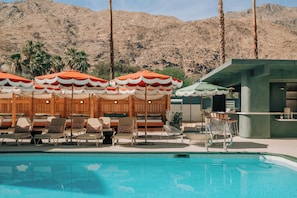 A poolside area with lounge chairs and umbrellas, a bar, and a mountain backdrop.