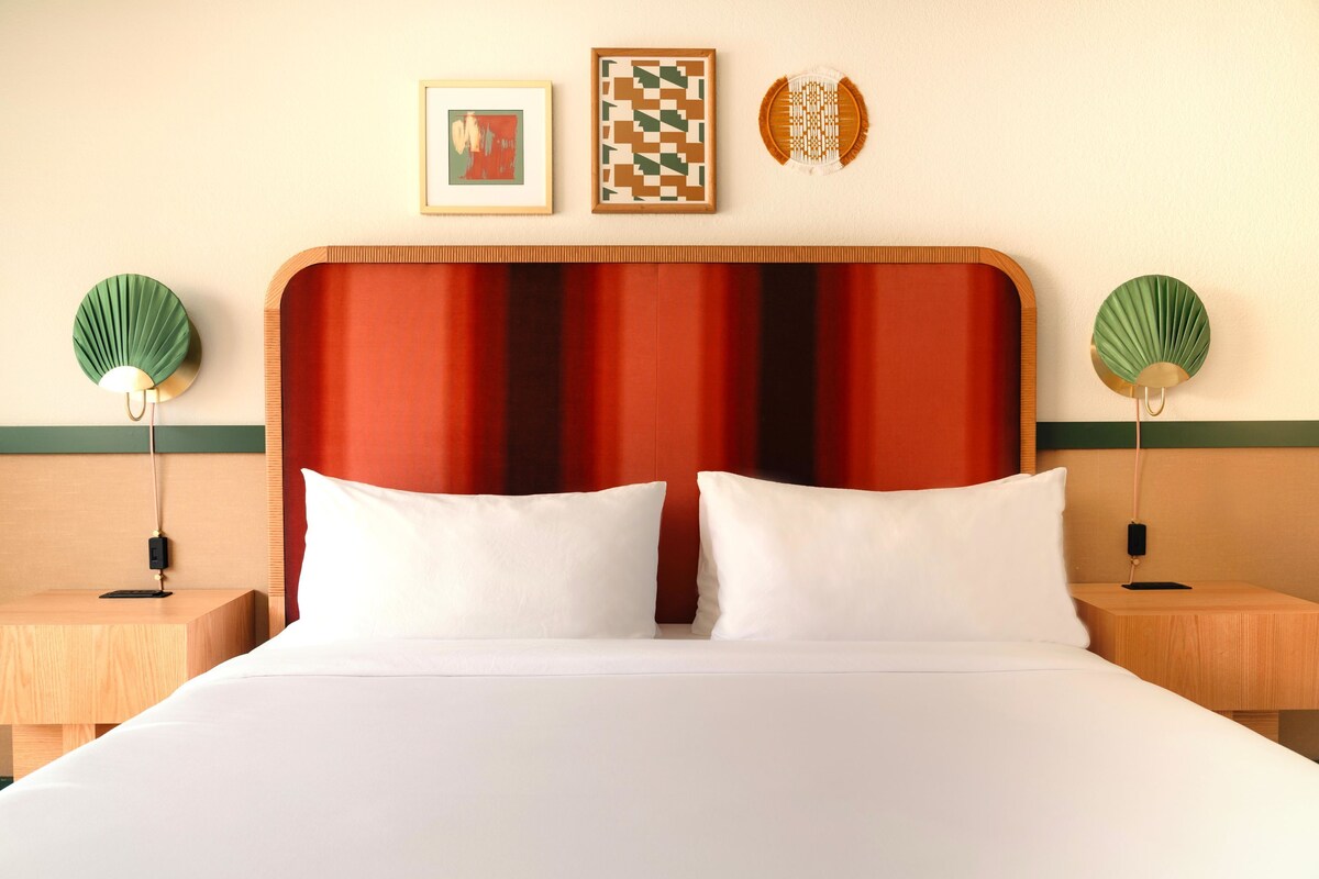 A hotel room with a large bed, two bedside tables, a headboard, and wall-mounted artwork.