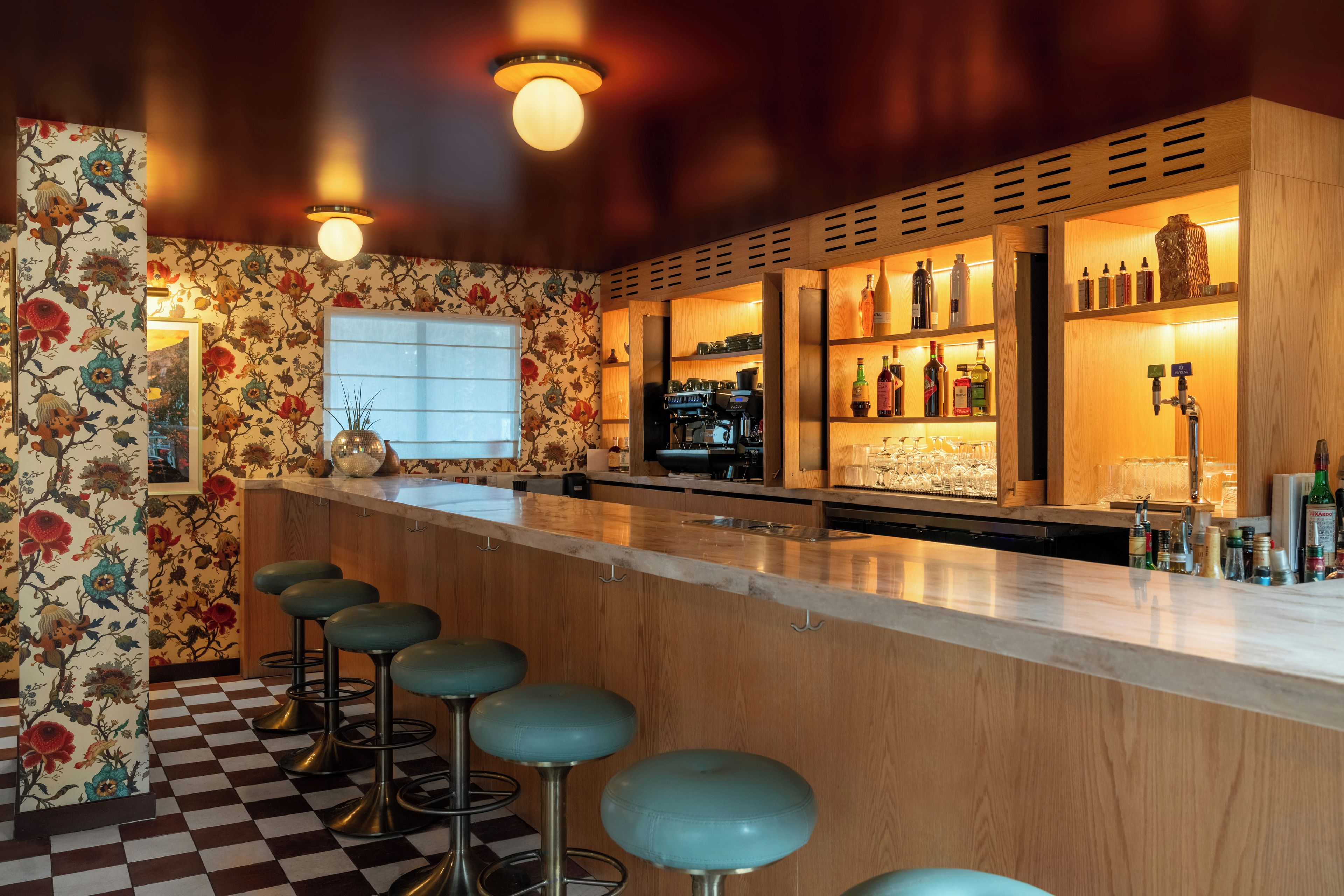 A bar area with a checkered floor, wooden bar counter, and stools.
