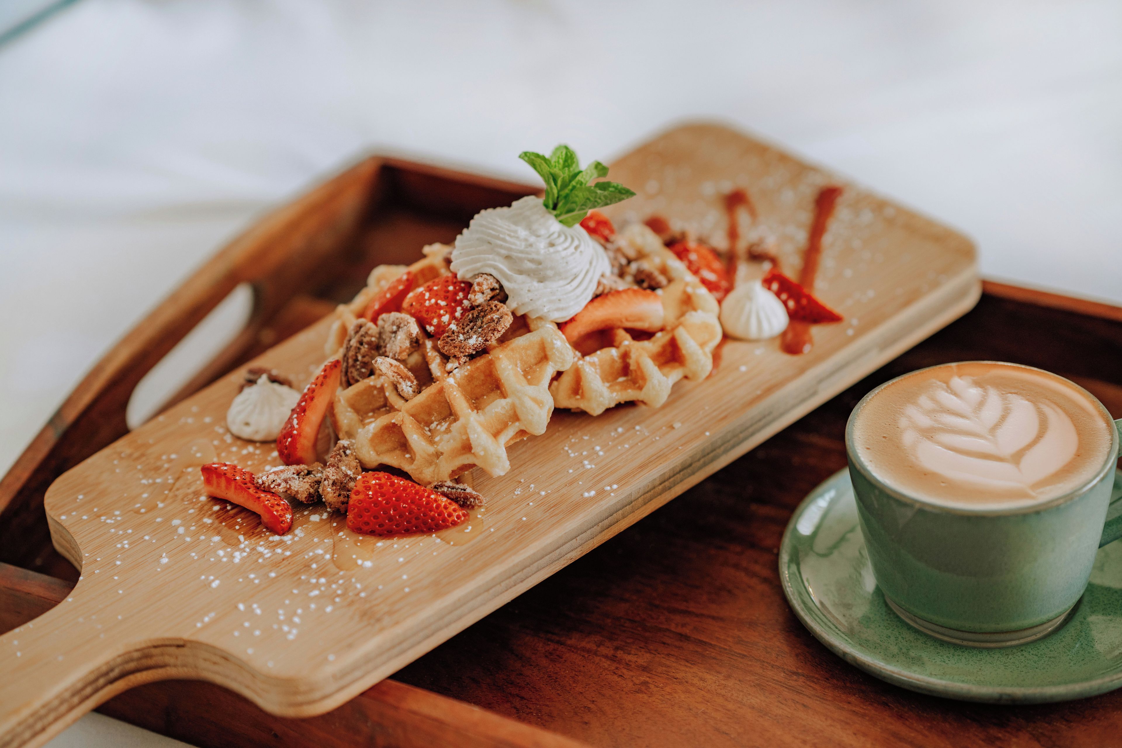 A wooden serving tray with waffles, strawberries, whipped cream, and pecans.