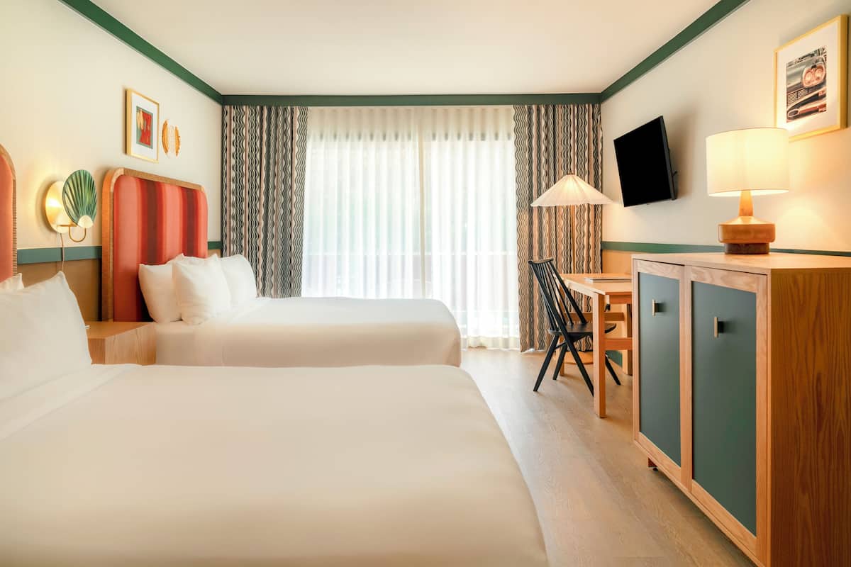 A hotel room with two beds, a desk, a television, and a cabinet.